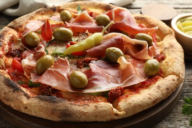 Photo of Tasty pizza with cured ham, olives, sun-dried tomato and pepper on wooden table, closeup