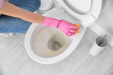 Woman cleaning toilet bowl in bathroom, closeup