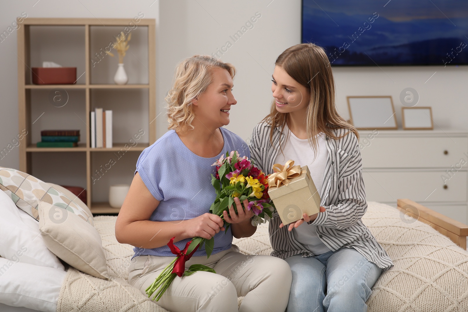 Photo of Young daughter congratulating her mom with flowers and gift at home. Happy Mother's Day