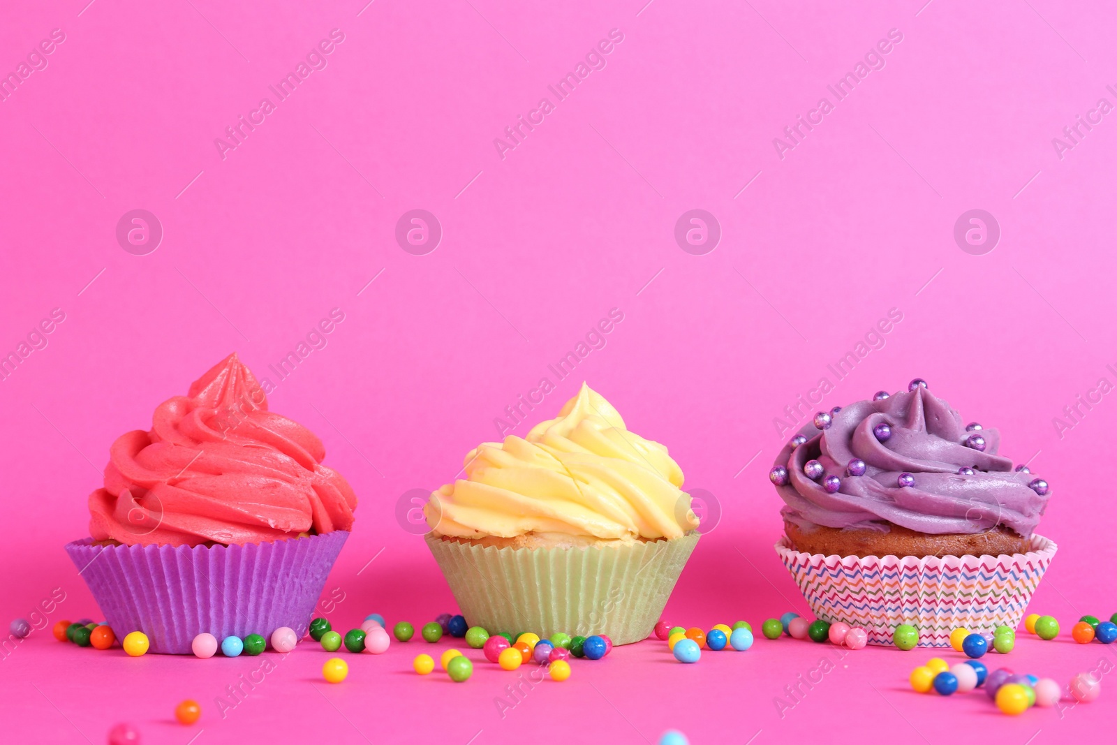 Photo of Delicious cupcakes with bright cream and sprinkles on pink background. Space for text