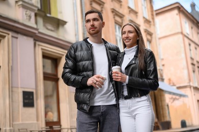 Photo of Lovely young couple with cups of coffee walking together on city street. Romantic date