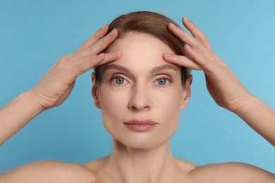 Photo of Woman massaging her face on turquoise background