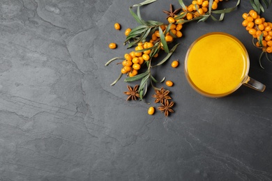 Photo of Sea buckthorn tea and fresh berries on grey table, flat lay. Space for text