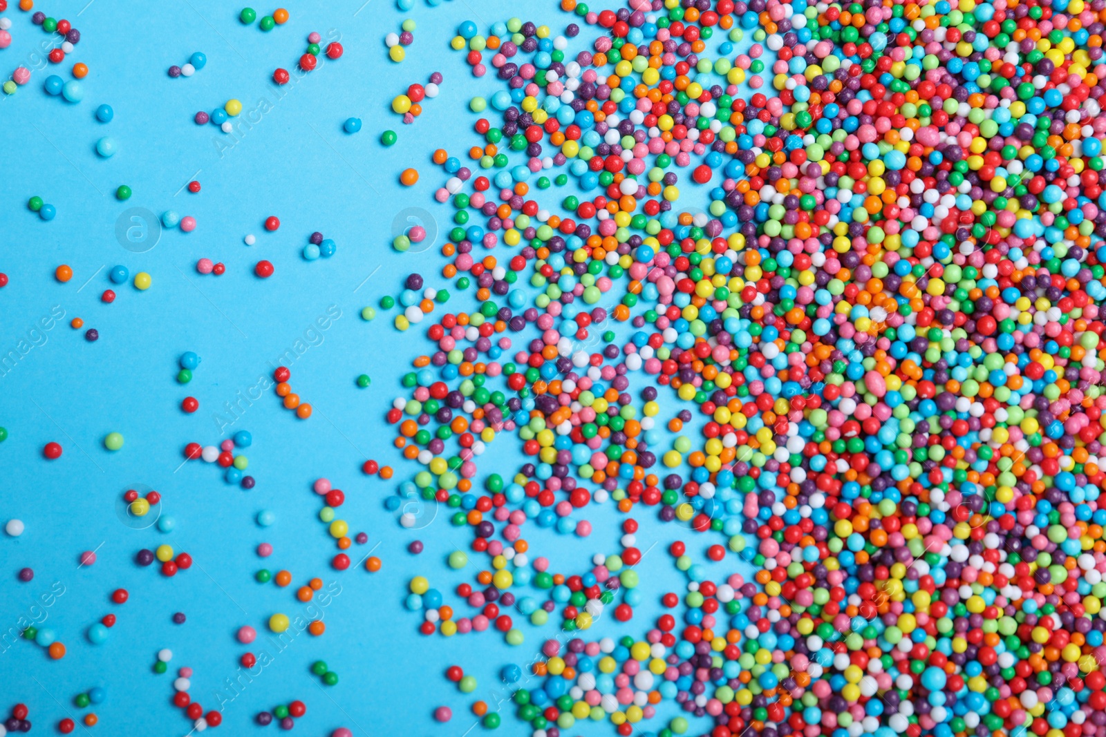 Photo of Colorful sprinkles on light blue background, flat lay. Confectionery decor