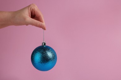 Photo of Woman holding blue Christmas ball on pink background, closeup. Space for text