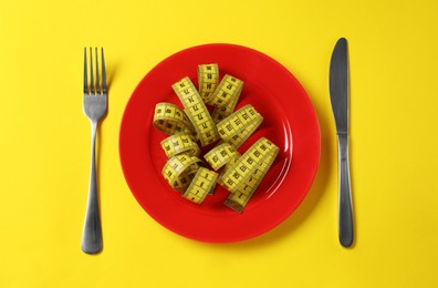 Photo of Plate, cutlery and measuring tape on yellow background, flat lay. Diet concept