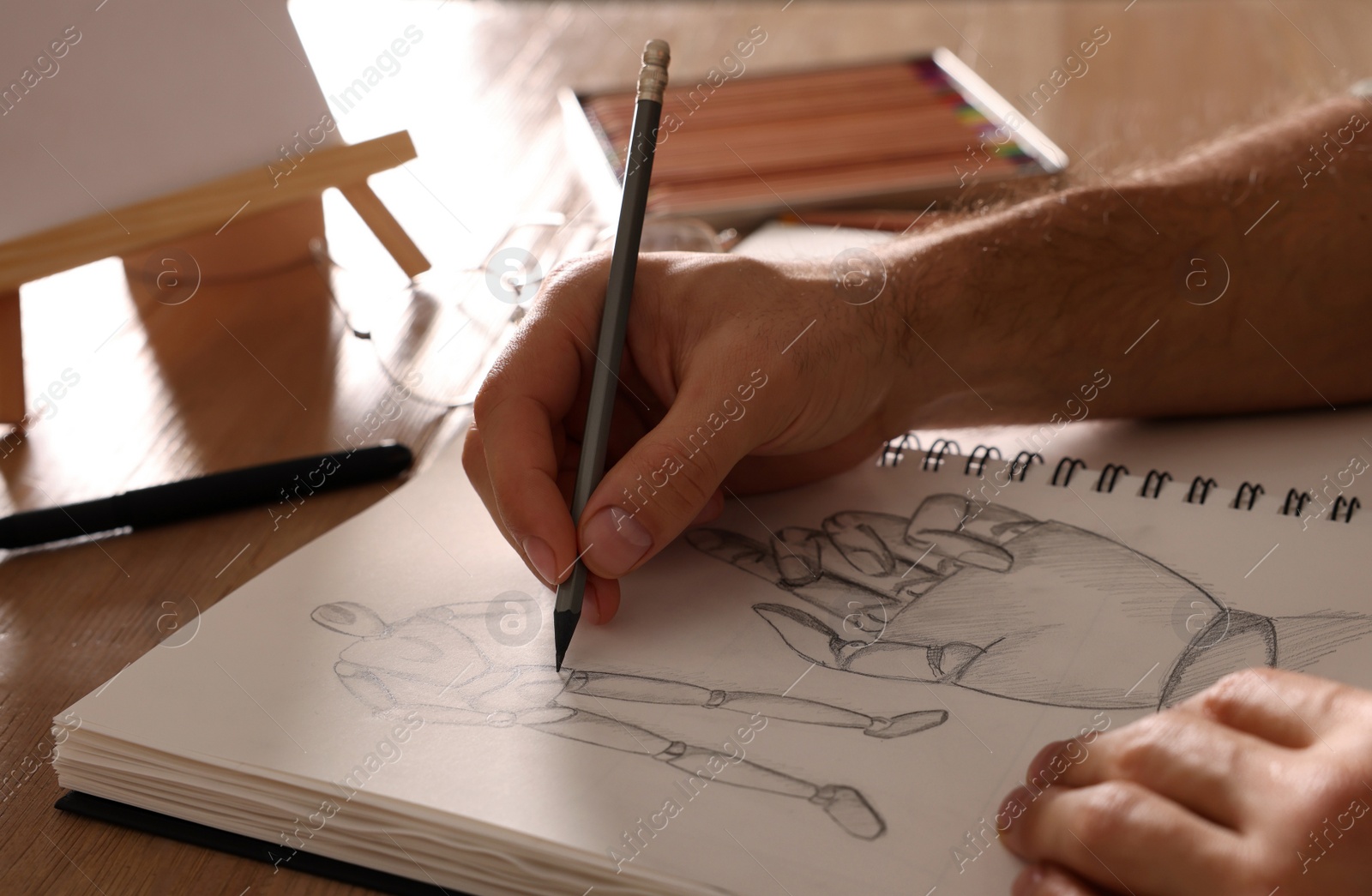 Photo of Man drawing in sketchbook with pencil at wooden table, closeup