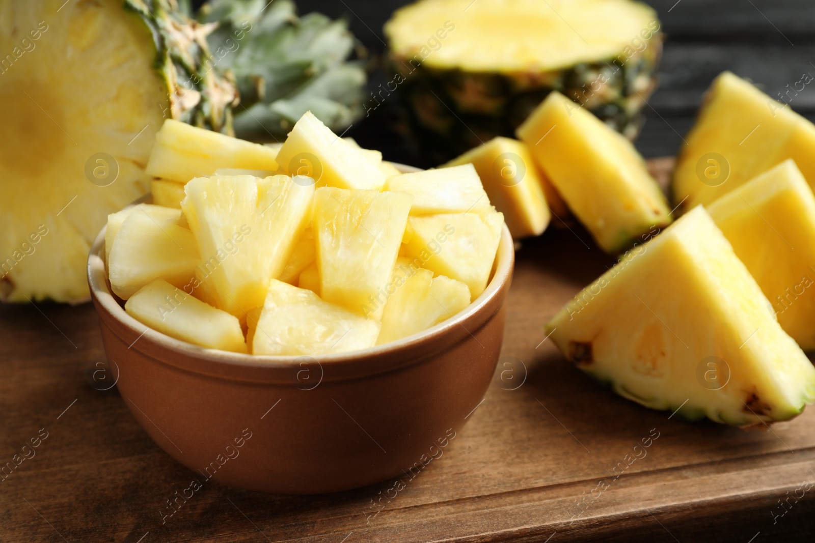 Photo of Bowl with fresh sliced pineapple on wooden board