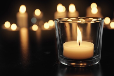 Burning candle on table in darkness, space for text. Funeral symbol