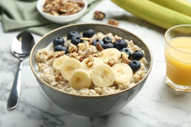 Tasty oatmeal with banana, blueberries, walnuts and milk served in bowl on white marble table