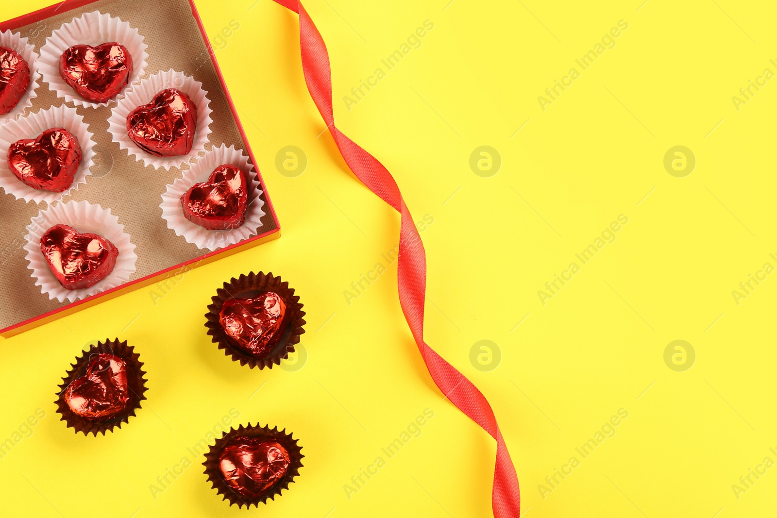 Photo of Heart shaped chocolate candies and ribbon on yellow background, flat lay. Space for text