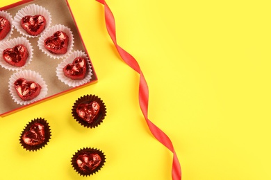 Photo of Heart shaped chocolate candies and ribbon on yellow background, flat lay. Space for text