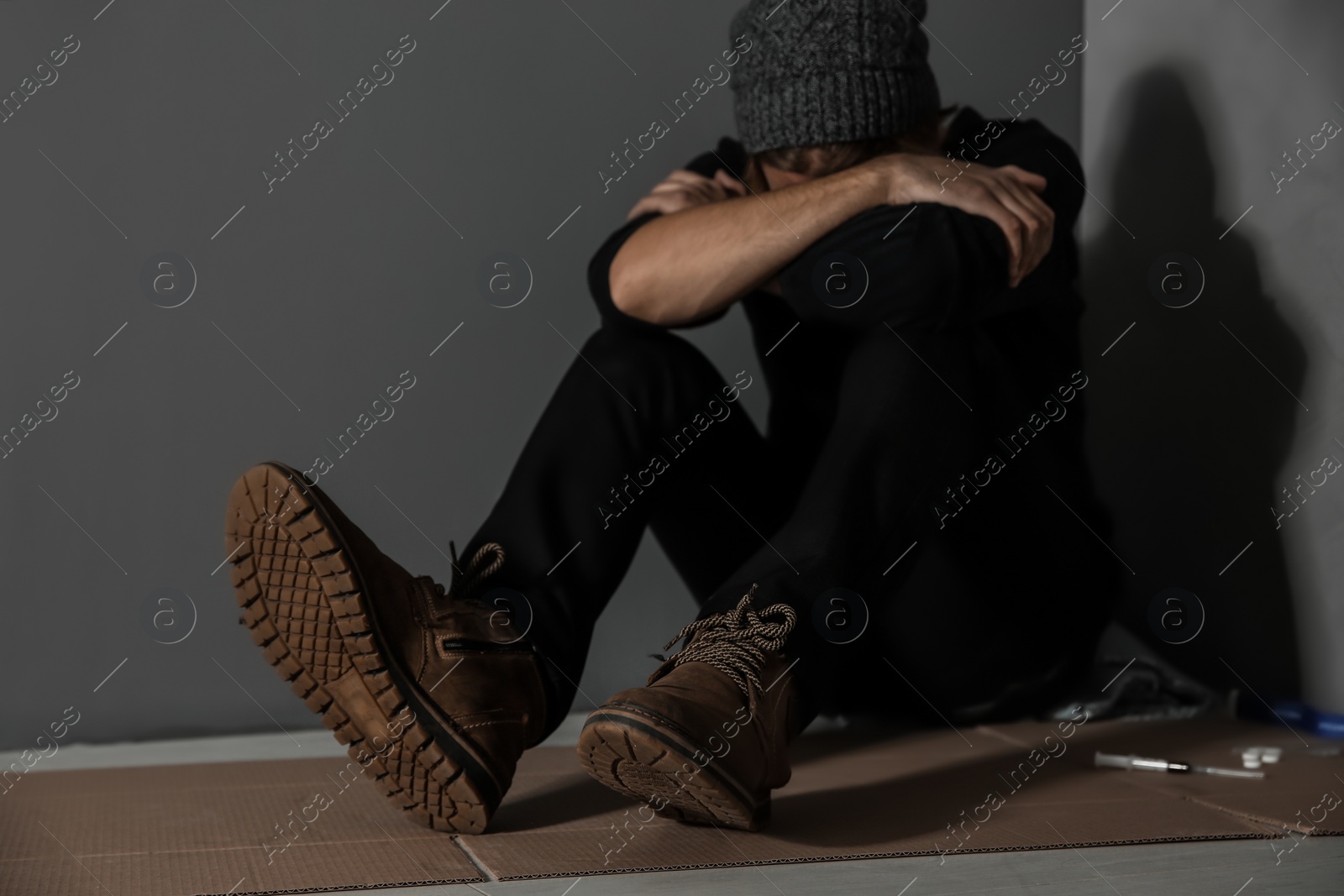 Photo of Stoned drug addict sitting on floor near grey wall