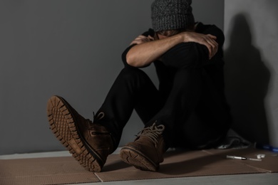 Photo of Stoned drug addict sitting on floor near grey wall