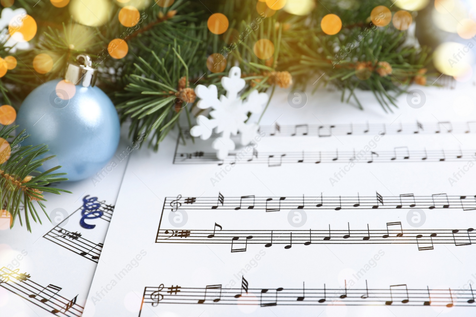 Photo of Fir branches, decorative snowflake and light blue balls on Christmas music sheets, closeup