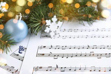 Photo of Fir branches, decorative snowflake and light blue balls on Christmas music sheets, closeup