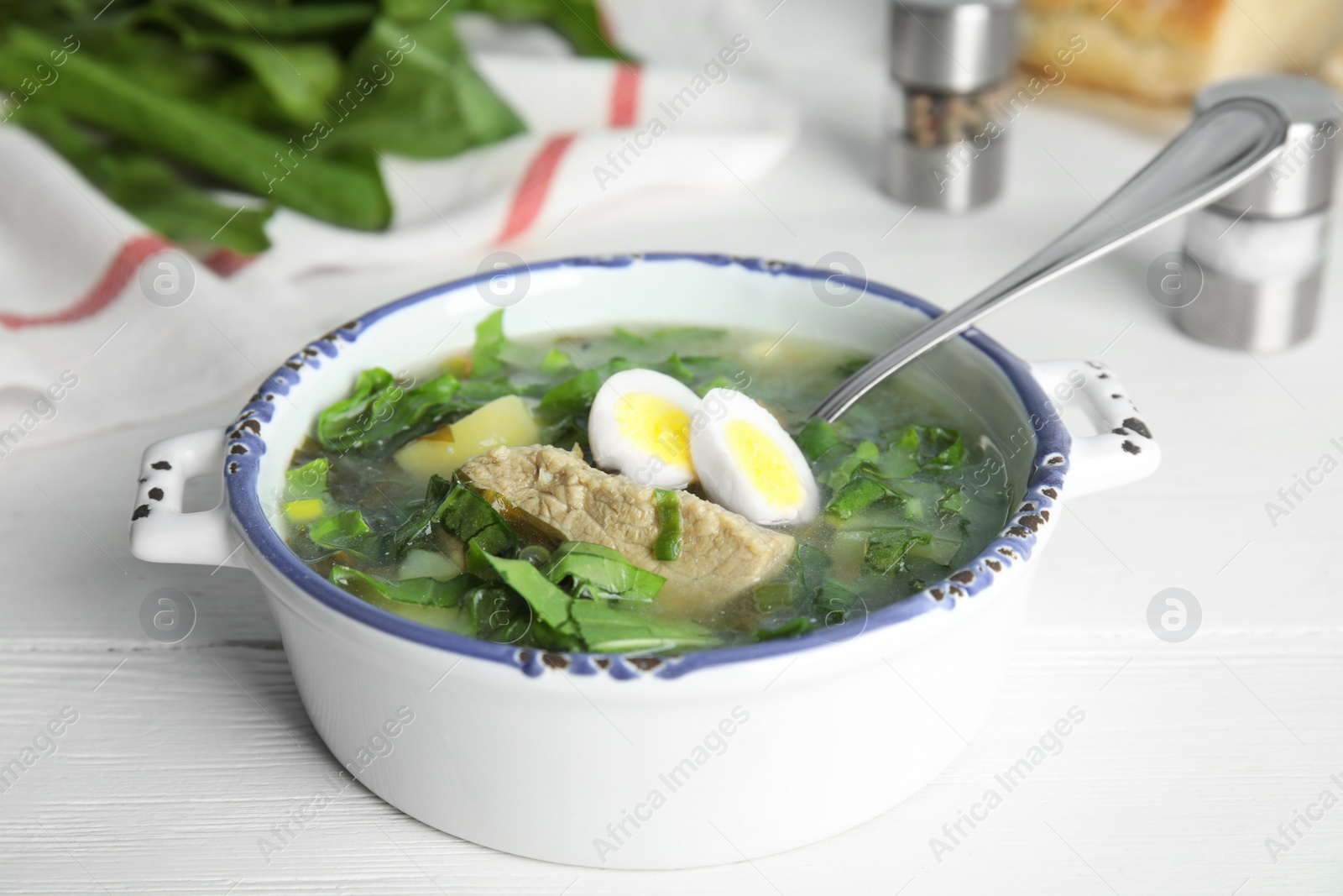 Photo of Delicious sorrel soup with meat and eggs served on white wooden table