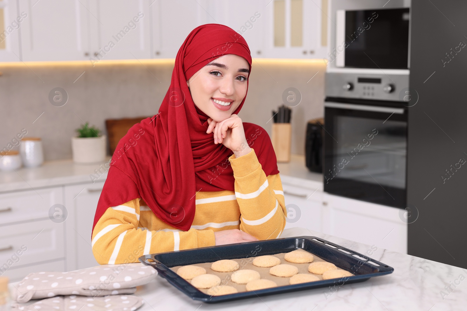 Photo of Portrait of Muslim woman near tray with cookies at white table in kitchen