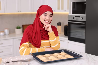 Portrait of Muslim woman near tray with cookies at white table in kitchen