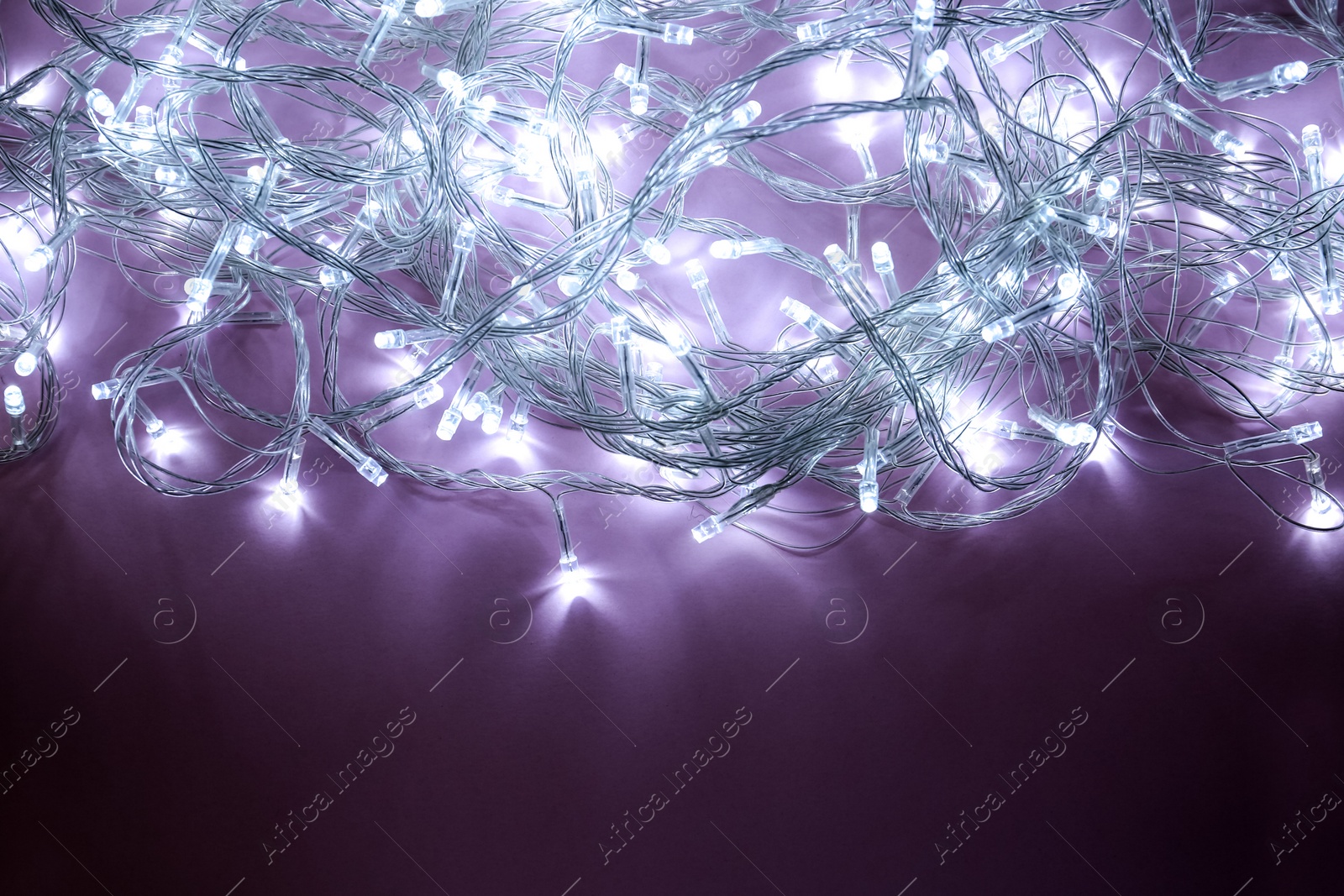 Photo of Glowing Christmas lights on violet background, top view. Space for text