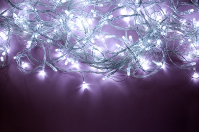 Glowing Christmas lights on violet background, top view. Space for text