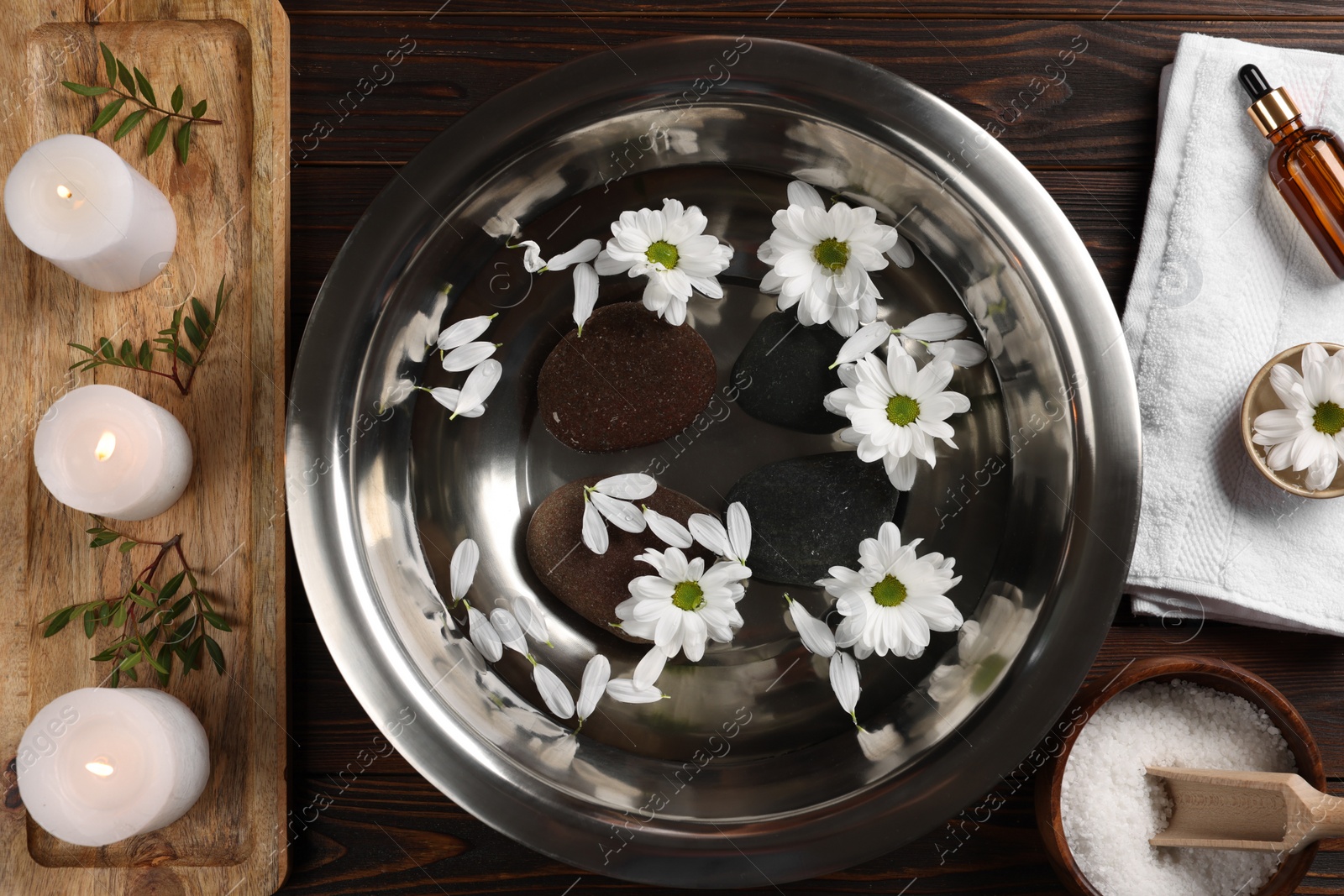 Photo of Bowl with water, flowers, stones and burning candles on wooden floor, flat lay. Pedicure procedure