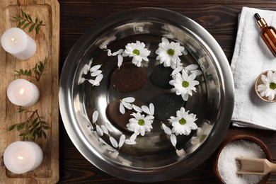 Photo of Bowl with water, flowers, stones and burning candles on wooden floor, flat lay. Pedicure procedure