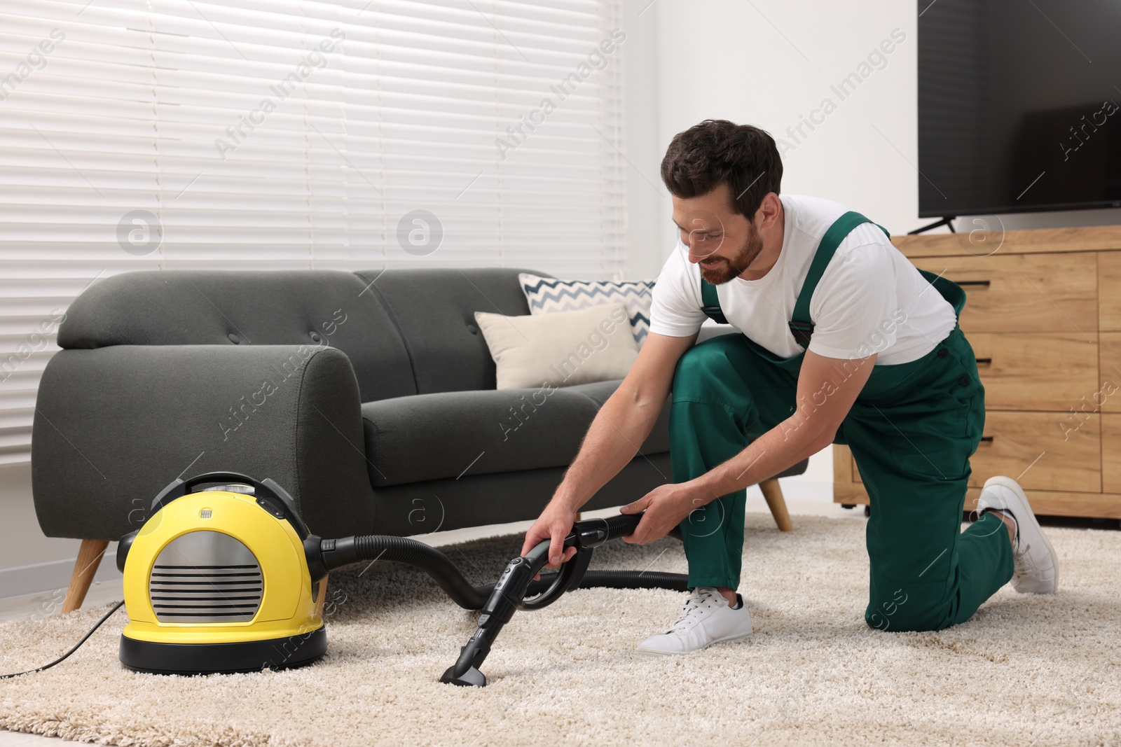 Photo of Dry cleaner's employee hoovering carpet with vacuum cleaner in room