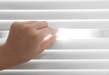 Young woman opening window blinds, closeup. Space for text