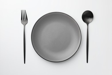 Empty plate, fork and spoon on white background, top view