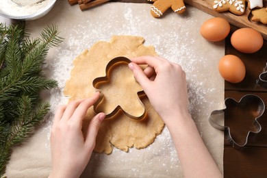 Photo of Woman making Christmas cookies with cutters at wooden table, top view