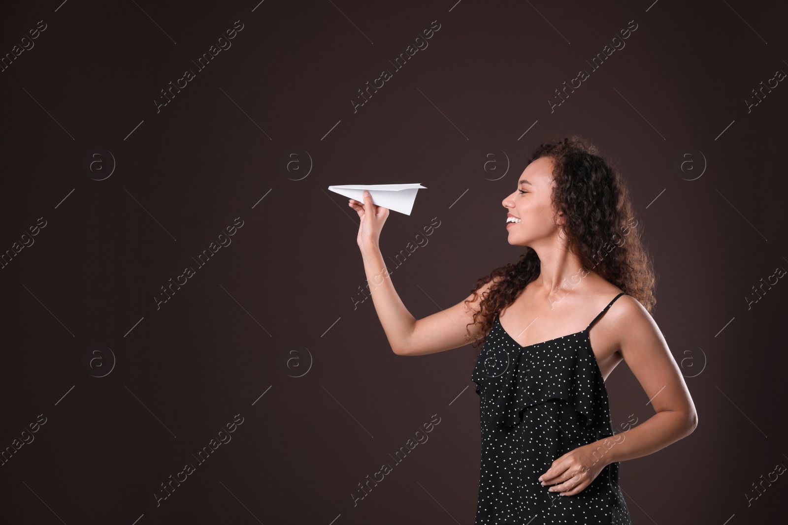 Photo of Beautiful African-American woman playing with paper plane on brown background. Space for text