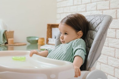 Cute little baby sitting in high chair indoors