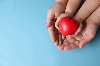 Father and his child holding red decorative heart on light blue background, top view. Space for text