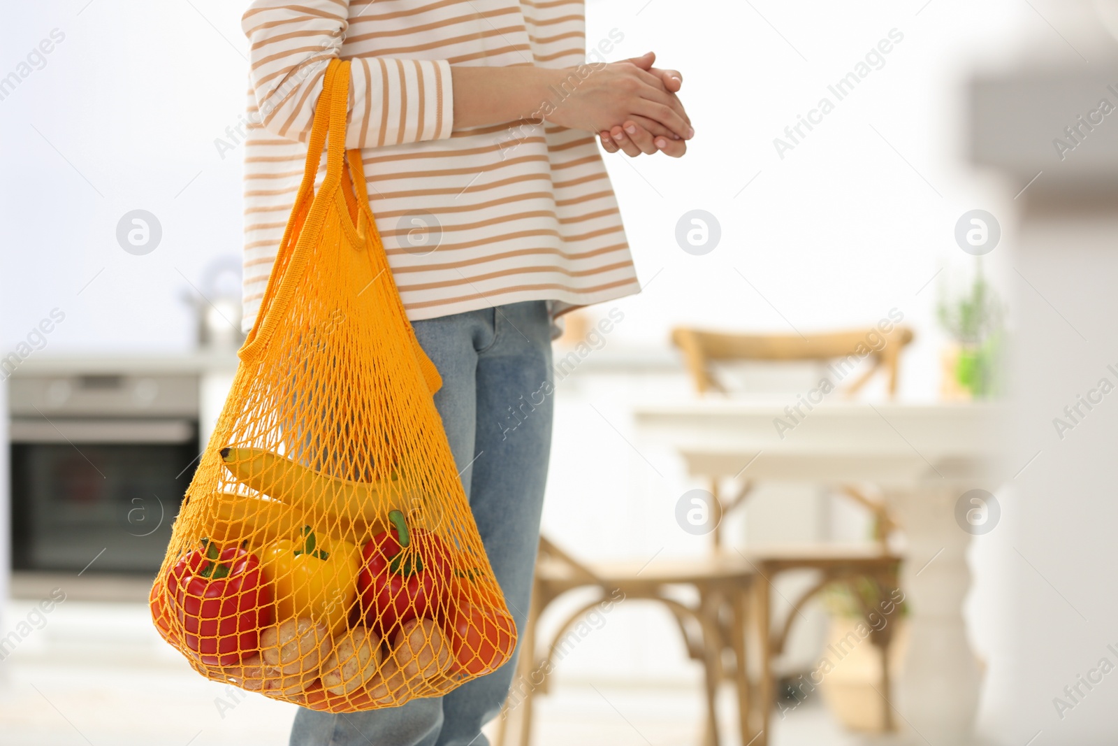 Photo of Woman with net bag full of fruits and vegetables in kitchen, closeup