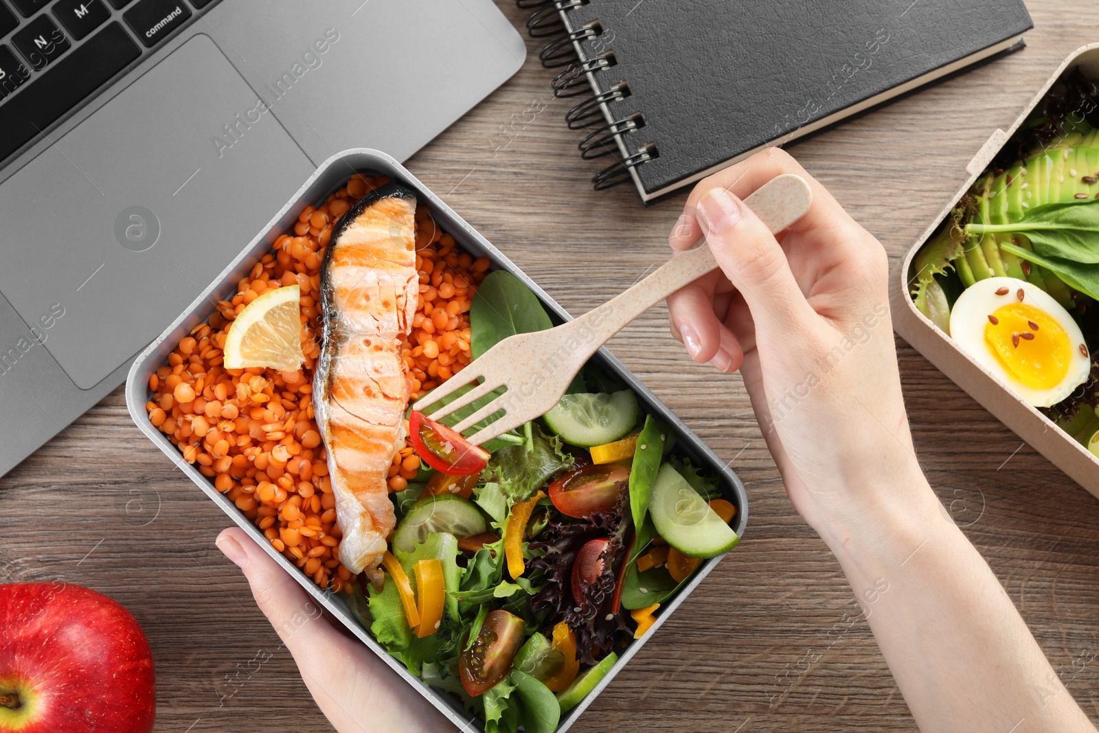 Photo of Woman eating healthy products high in vegetable fats near laptop at wooden table, top view