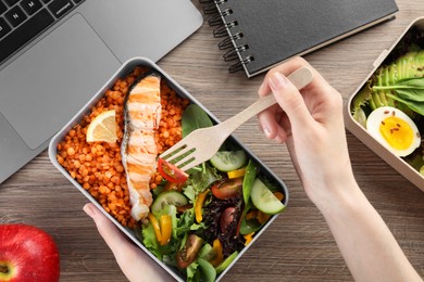 Woman eating healthy products high in vegetable fats near laptop at wooden table, top view