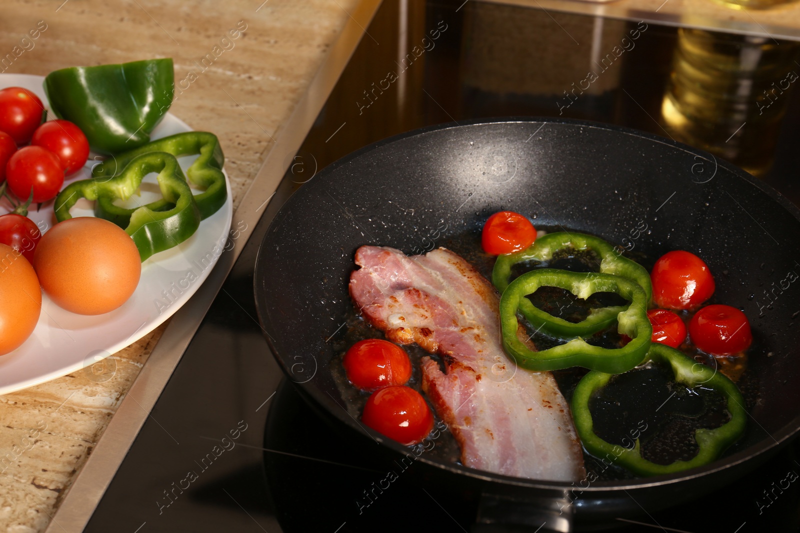 Photo of Cooking bacon with tomatoes and pepper in frying pan. Ingredients for breakfast