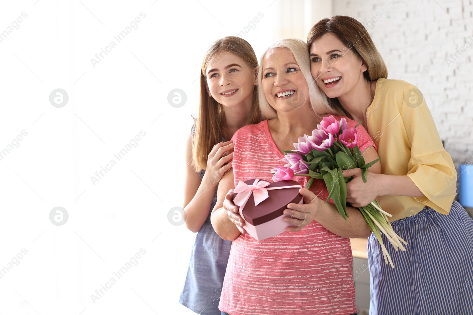 Photo of Young woman with daughter congratulating mature family member at home. Happy Mother's Day