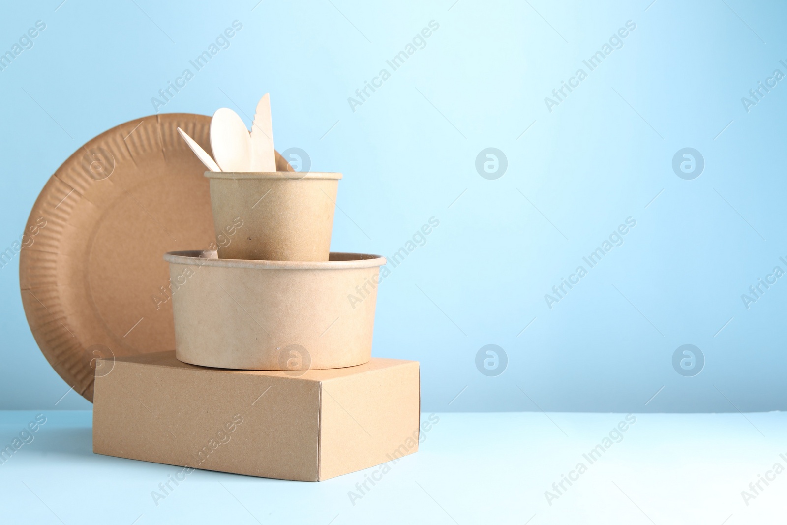 Photo of Eco friendly food packaging. Paper containers and tableware on white table against light blue background, space for text