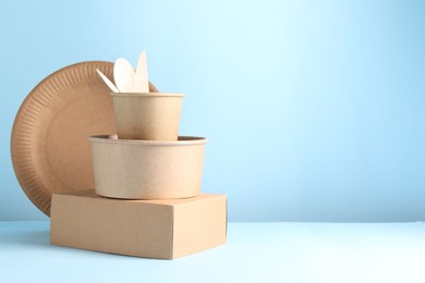 Photo of Eco friendly food packaging. Paper containers and tableware on white table against light blue background, space for text