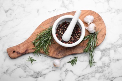 Photo of Sprigs of rosemary, mortar and garlic on white marble table, flat lay