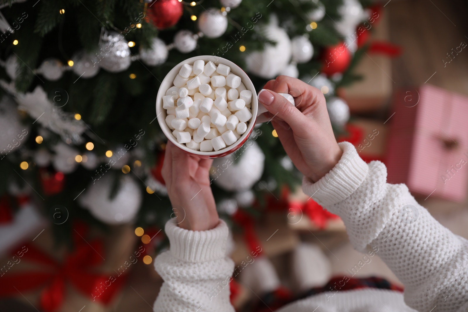 Photo of Woman with cup of delicious hot drink near Christmas tree at home, top view