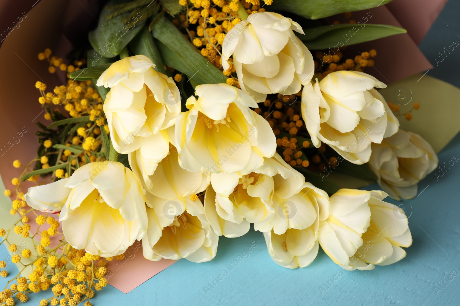 Photo of Bouquet with beautiful tulips and mimosa flowers on light blue wooden table