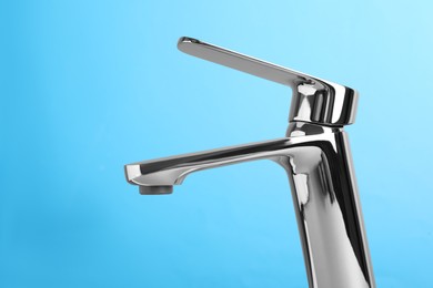 Single handle water tap on light blue background, closeup