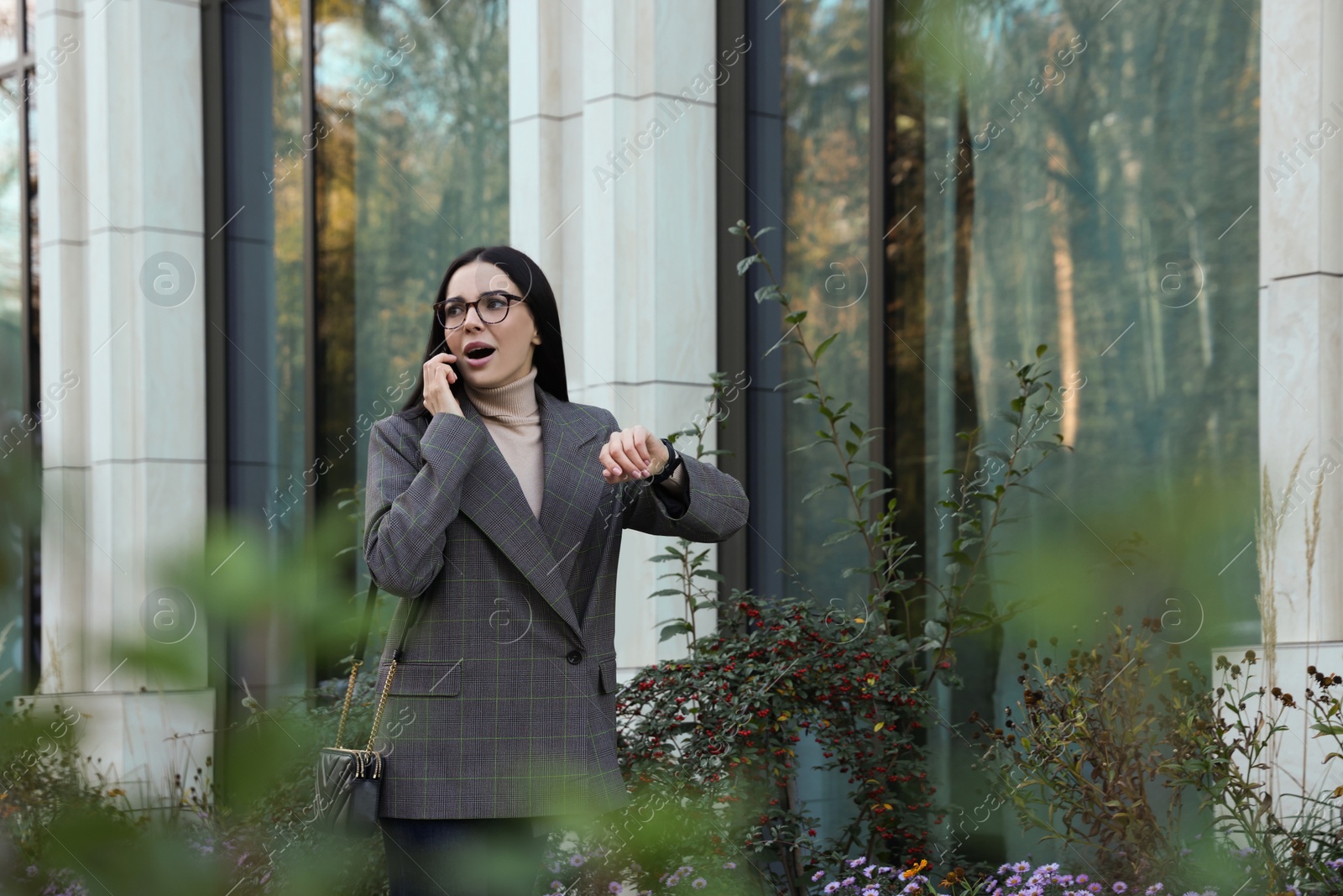 Photo of Emotional woman checking time while talking on smartphone outdoors. Being late concept