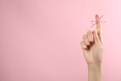 Photo of Woman showing index finger with tied bow as reminder on pink background, closeup. Space for text