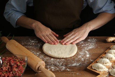 Photo of Woman kneading dough for gyoza at wooden table, closeup