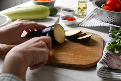 Photo of Cooking delicious ratatouille. Woman cutting fresh eggplant at white wooden table, closeup