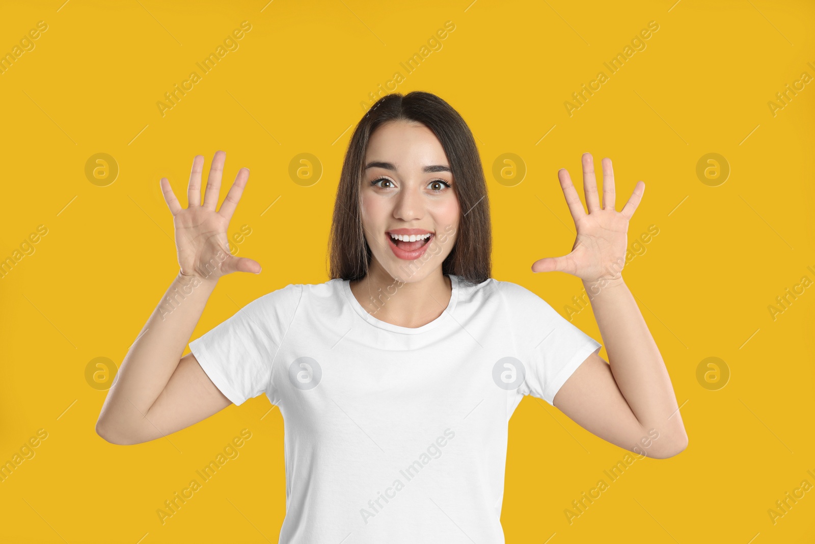 Photo of Woman in white t-shirt showing number ten with her hands on yellow background